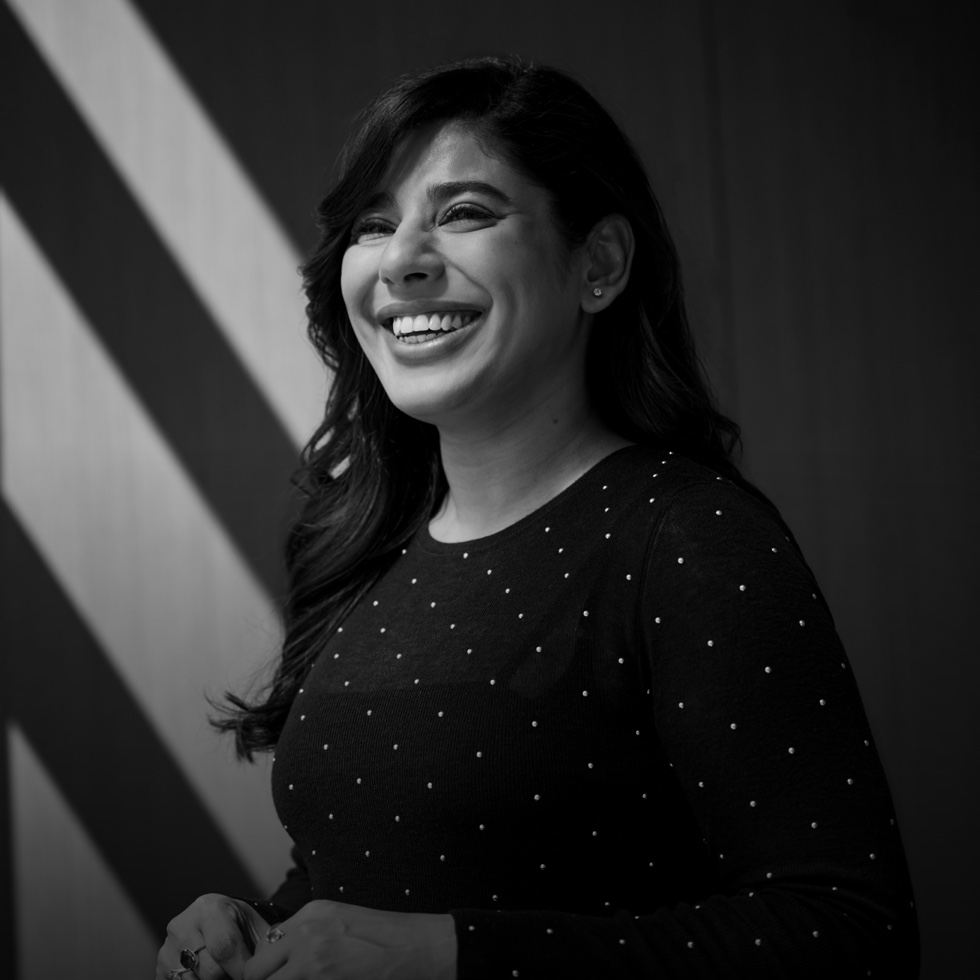 An engineer standing and smiling next to a sunlit wall.