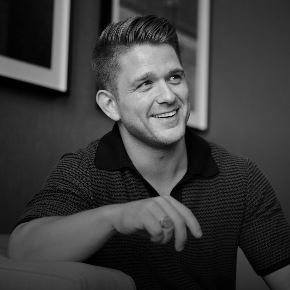 A product manager seated, smiling with two framed images on a wall behind him.