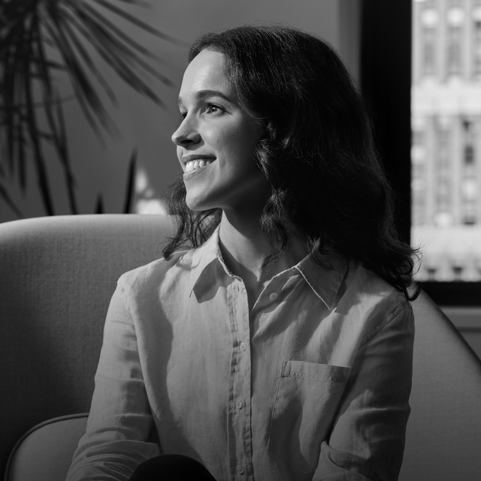  A sales representative smiling in a chair, looking to her right, a window and plant behind her. 