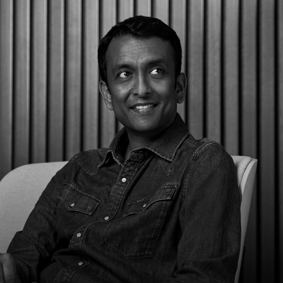 A marketing manager smiling, seated in a chair against a wood-paneled wall.