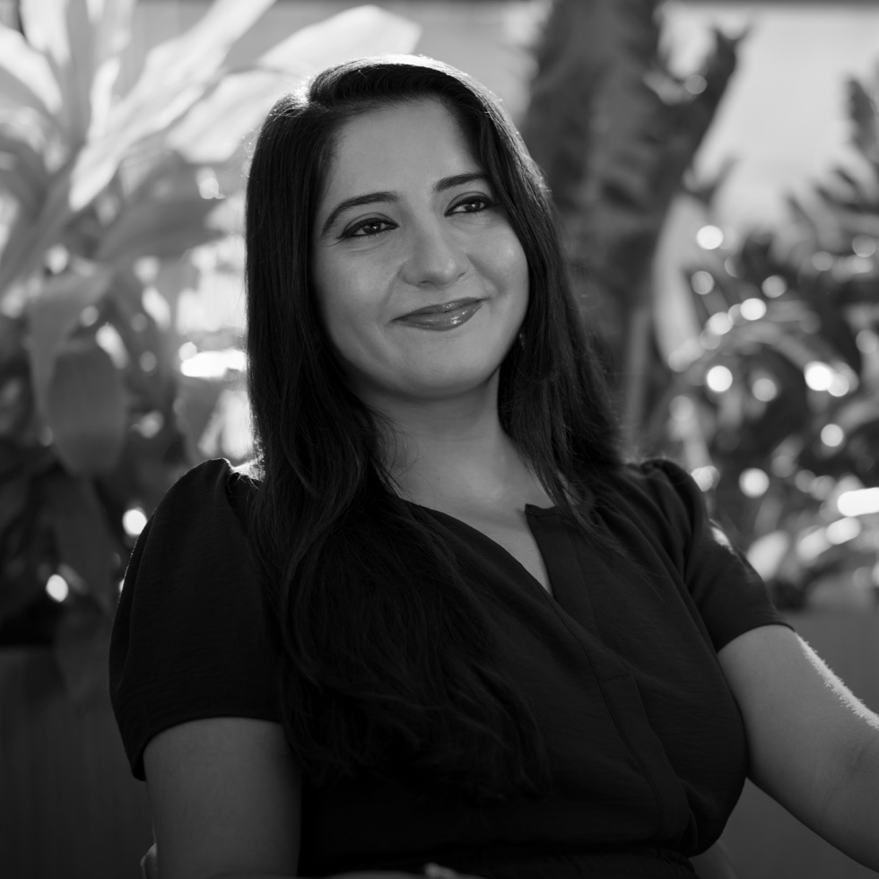 A data scientist with a large sunlit window and a wall of plants behind her.