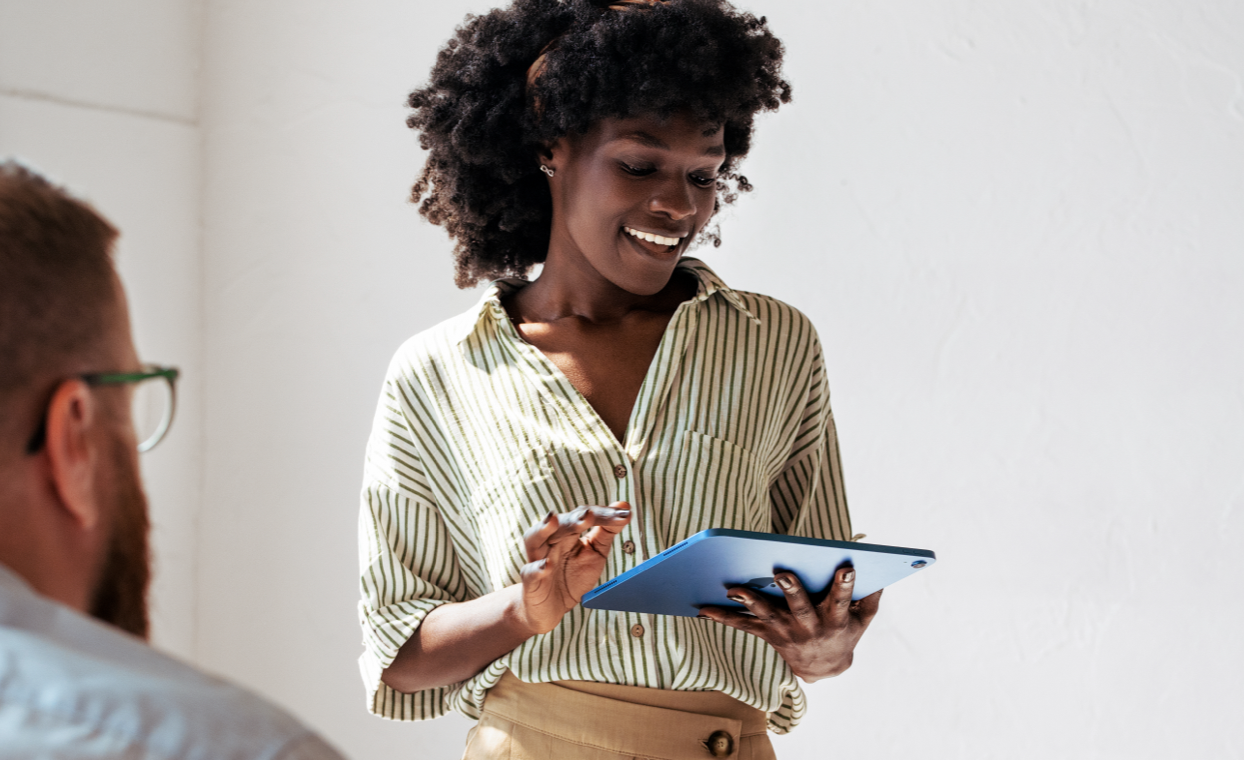 A person looks down at an iPad Pro with a smile, while a seated colleague looks on.