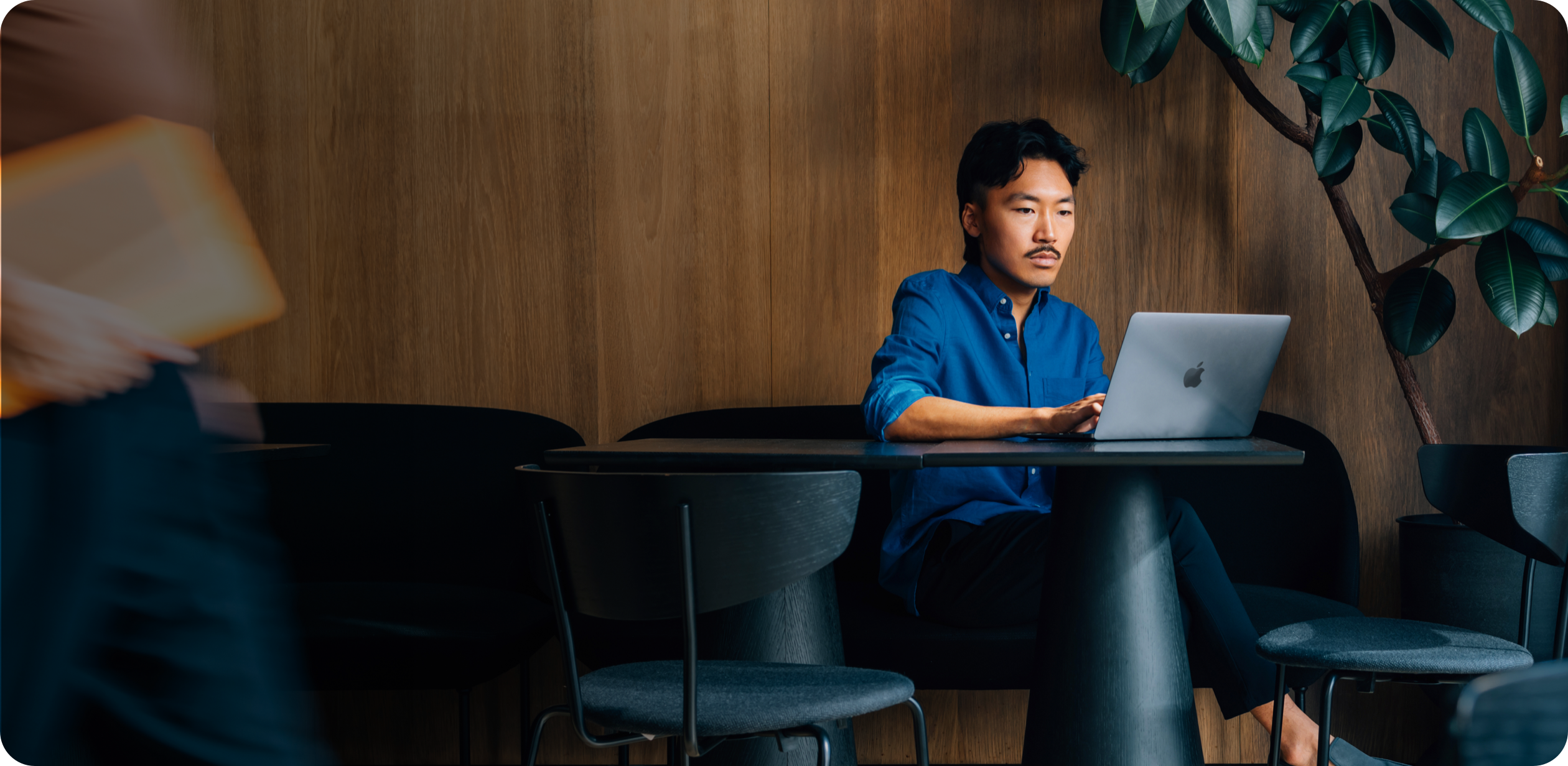 A data scientist works on a MacBook seated at a small table next to a sunlit window.