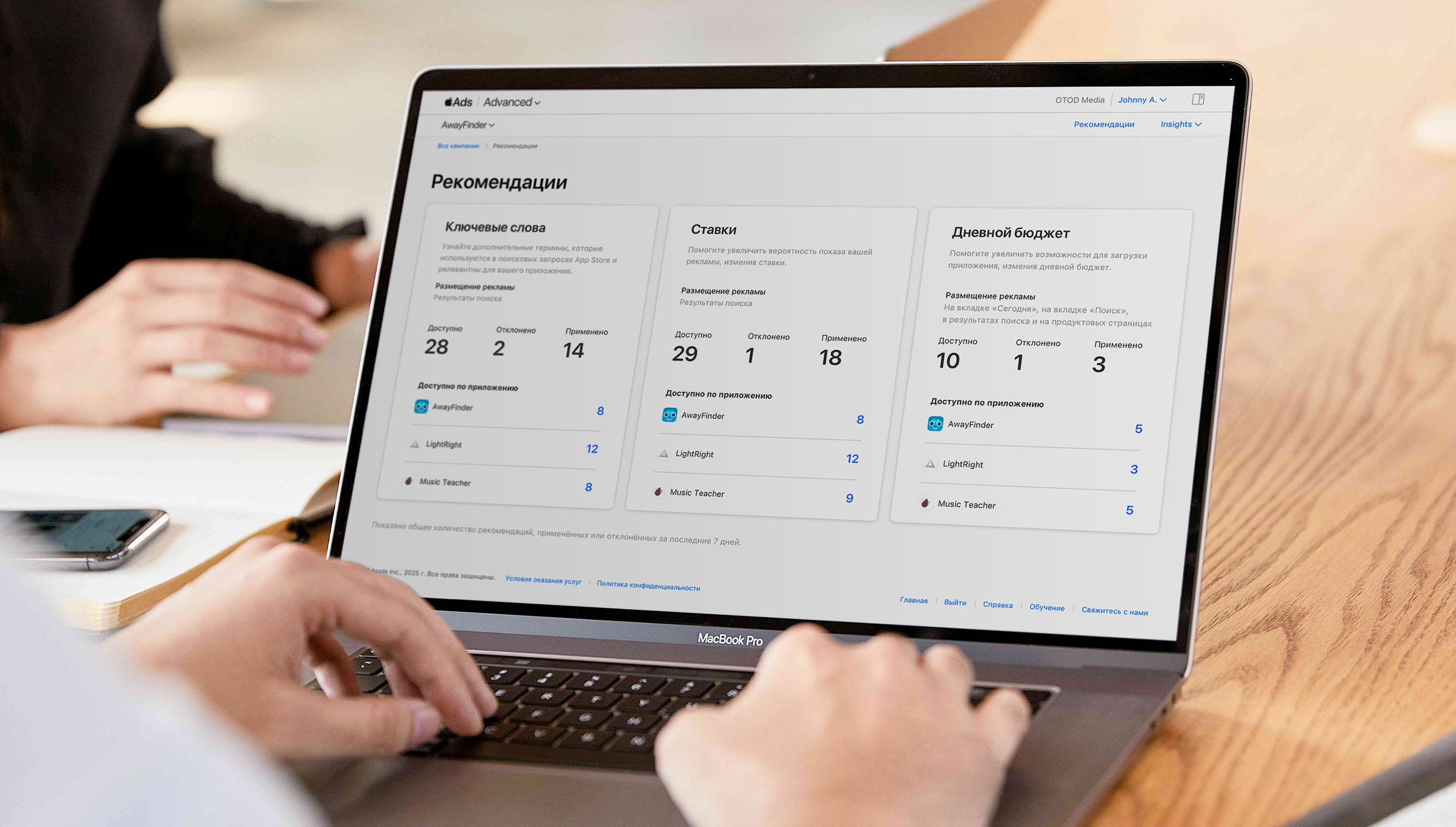 Крупный план рук пользователя, печатающего на клавиатуре MacBook. На экране открыта страница «Рекомендации» в Apple Ads, на которой показаны рекомендации, упорядоченные по ключевым словам, ставкам и дневному бюджету.
