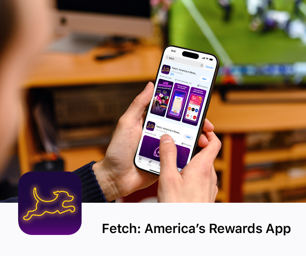 Eine Person hält ihr iPhone, während sie vor einem Fernseher sitzt, auf dem ein Football-Spiel läuft. Auf dem iPhone wird im App Store eine Suchergebnisanzeige für die Fetch App angezeigt.