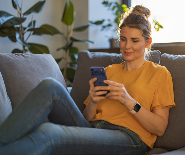 Persona in relax sul divano, che sorride mentre guarda il proprio iPhone.