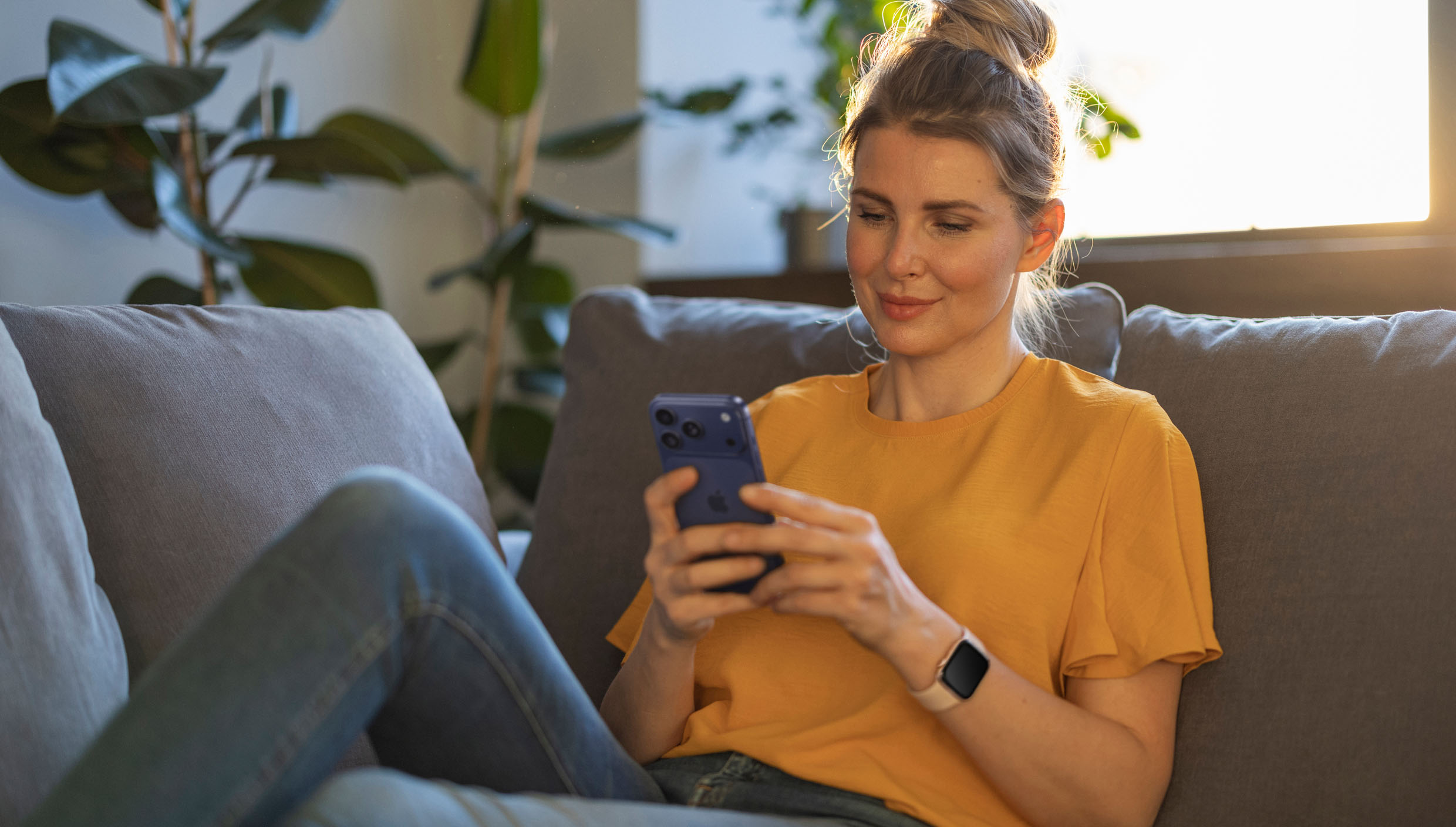 ソファでくつろぎながら、iPhoneを見て微笑んでいる人。