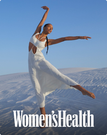 The cover of Women’s Health featuring an image of a woman in a white dress striking a dancer’s pose on white sand dunes. 