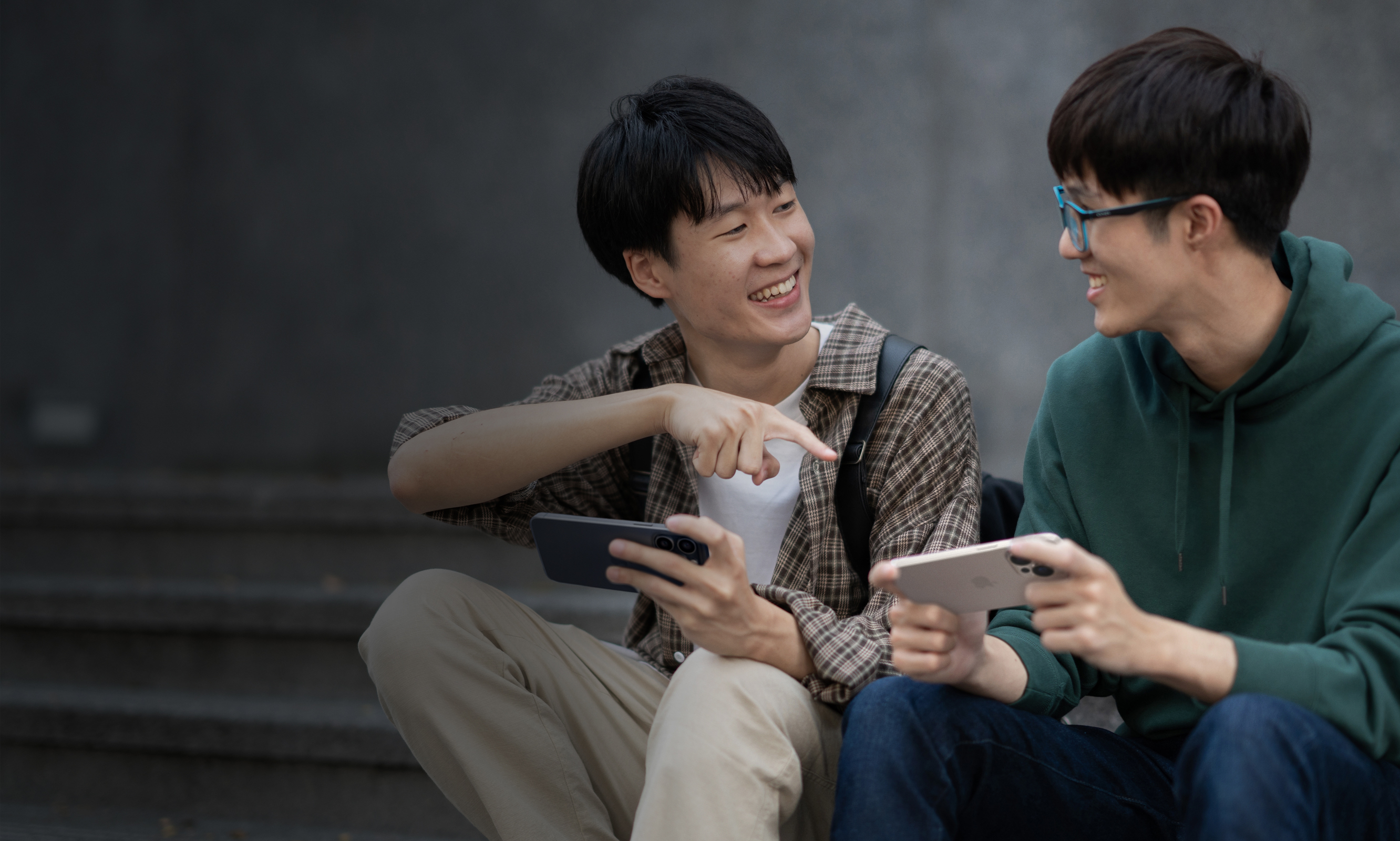 两个朋友微笑着在 iPhone 上玩游戏。