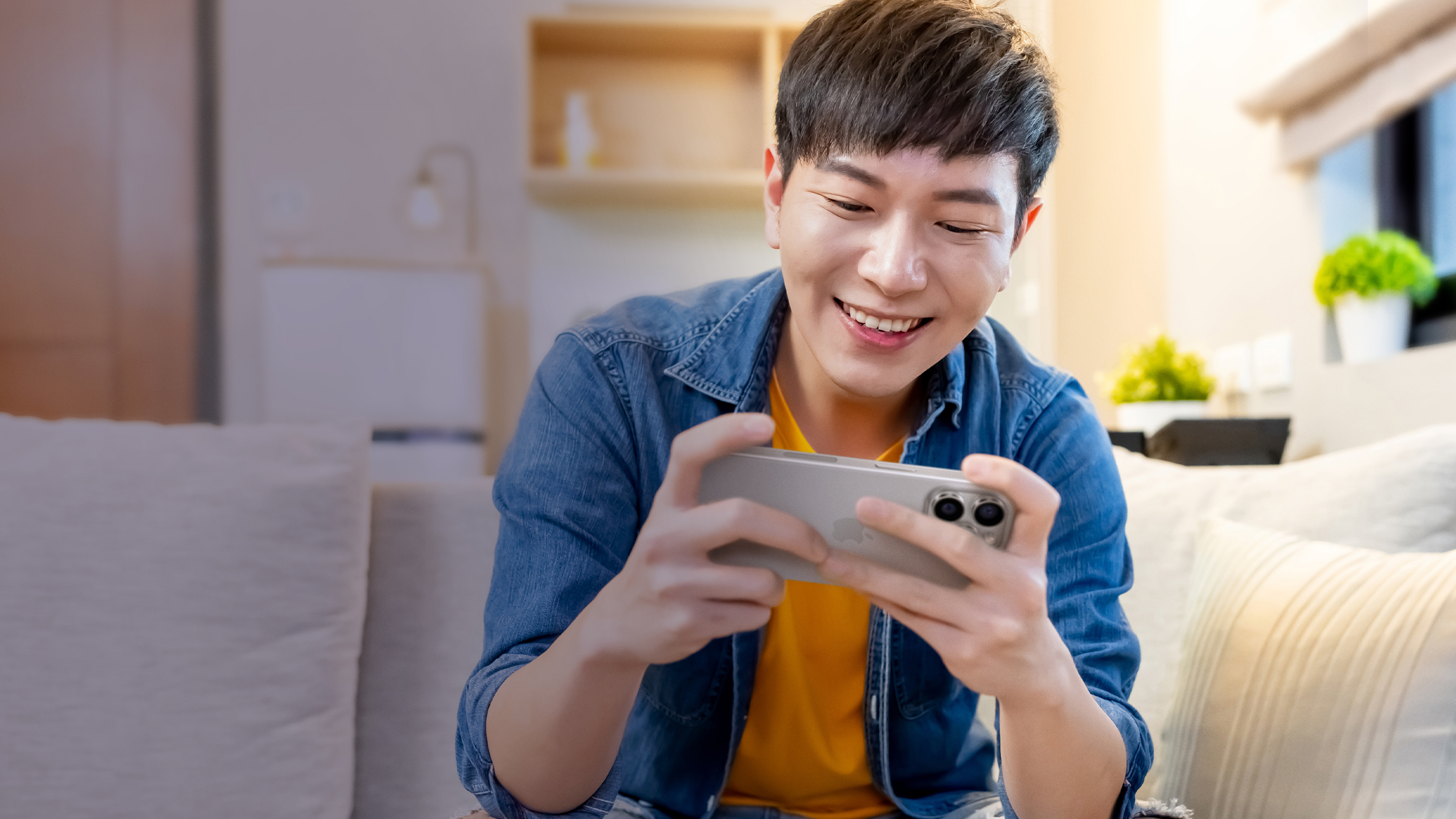 一个人面带笑容，放松地坐在沙发上，在 iPhone 上玩游戏。