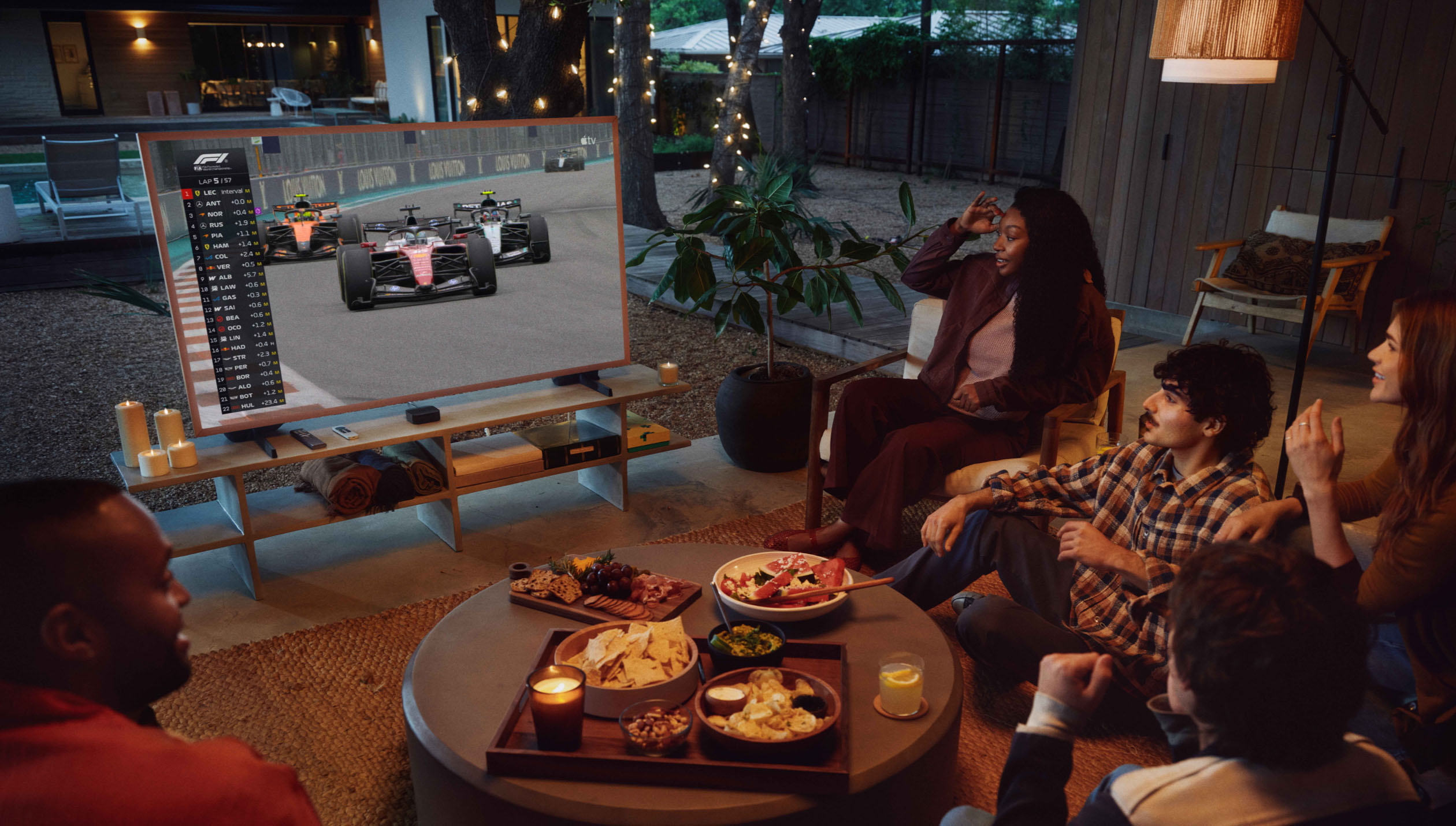 A group of friends intently watch an F1 race on Apple TV at an outdoor gathering.