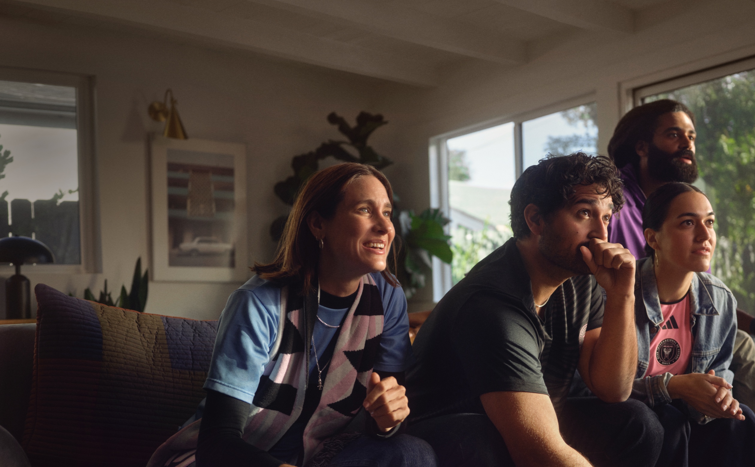 ソファに座り、Apple TVのMLSの試合を息をこらして見守る4人の友人グループ。 