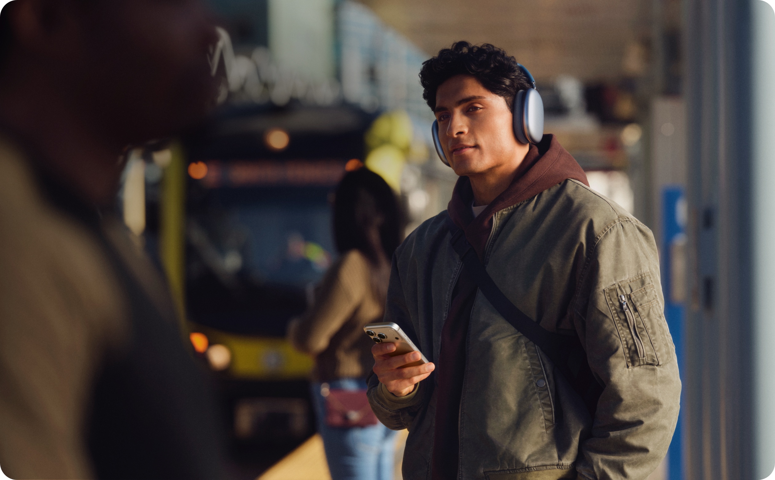 通勤電車が近づく駅のプラットフォームに立っている人。手にiPhoneを持っている。