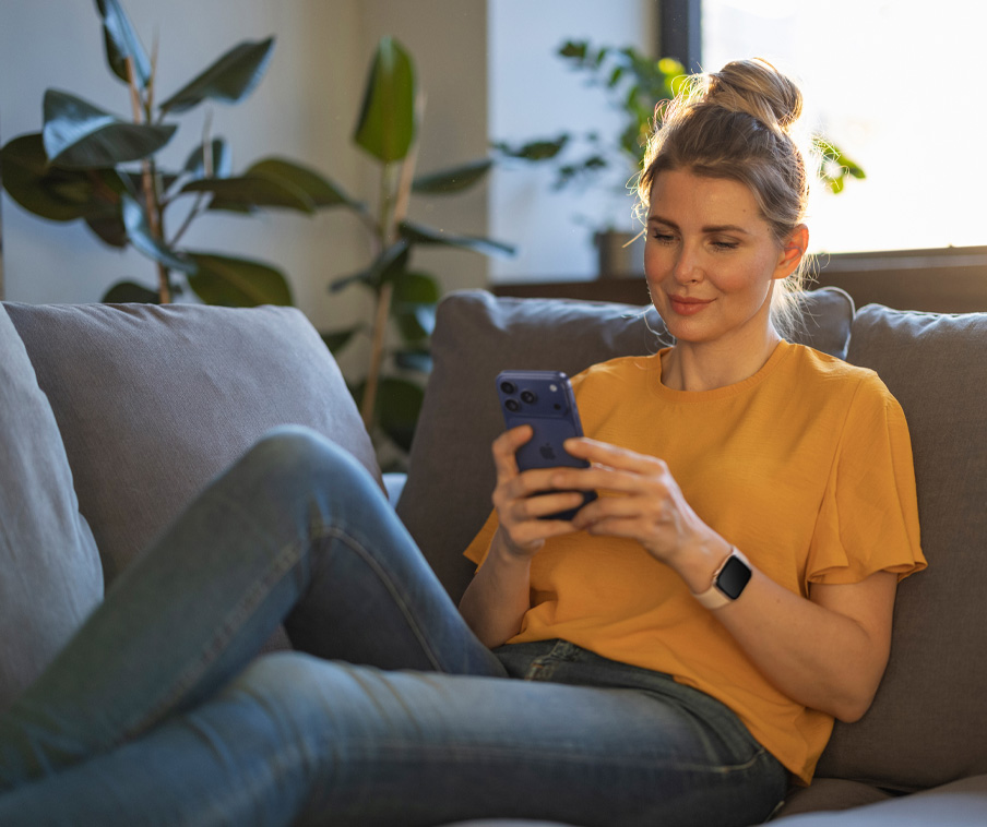 Persona in relax sul divano, che sorride mentre guarda il proprio iPhone.