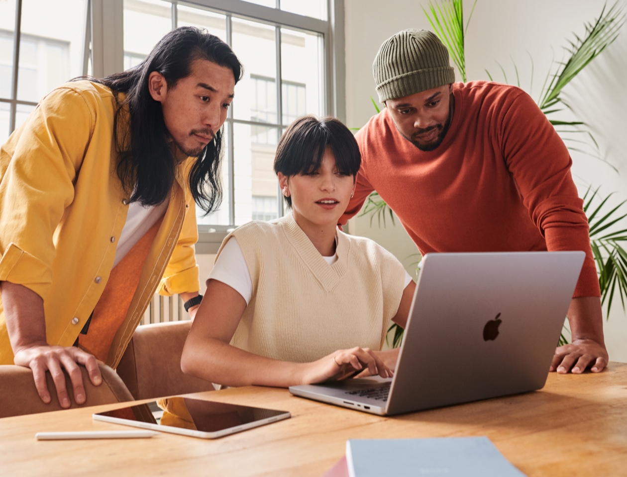 Three people gathered around a MacBook on a table, looking at the screen together