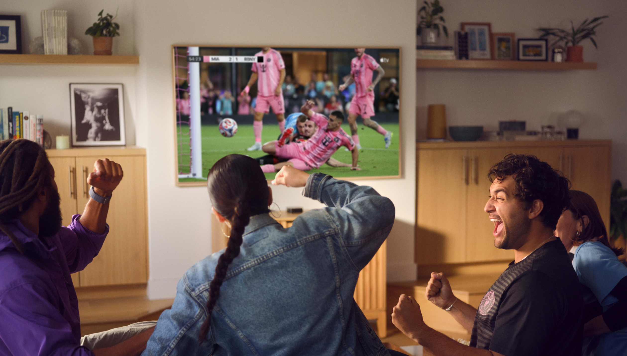 Un groupe de quatre personnes assises sur un canapé, en train d’encourager leur équipe en regardant un match de la MLS à la télévision.