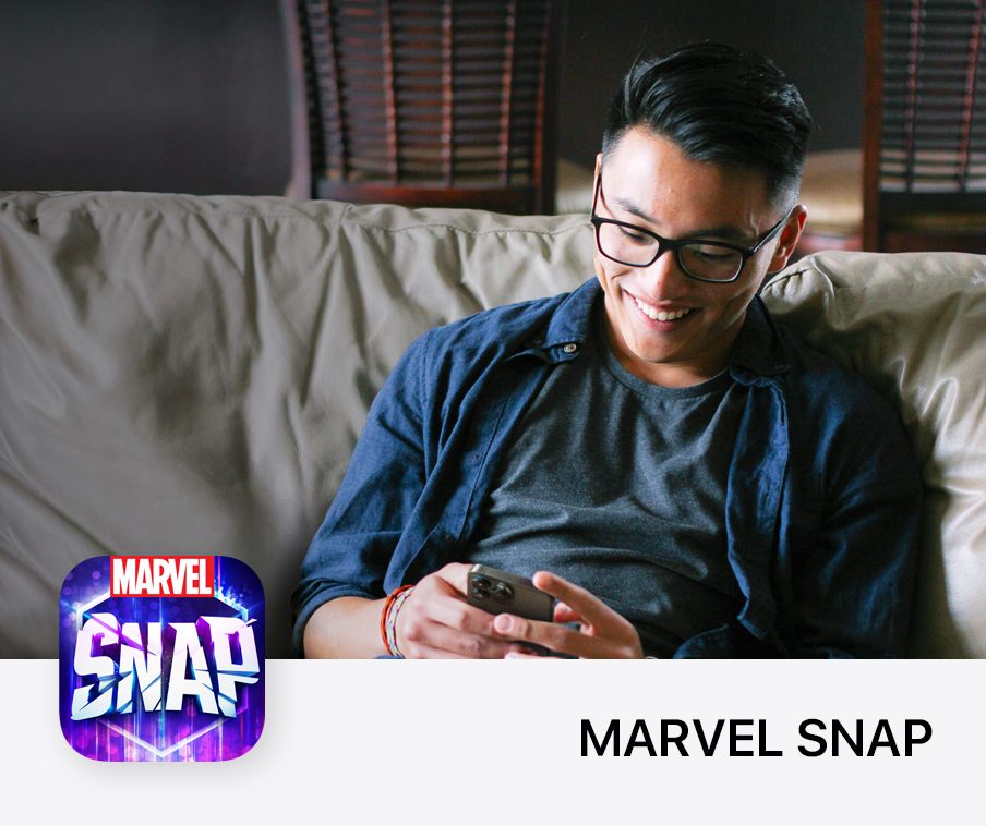 一位男士坐在沙发上，面带微笑，低头看着 iPhone。他的下方是 MARVEL SNAP app 图标。 