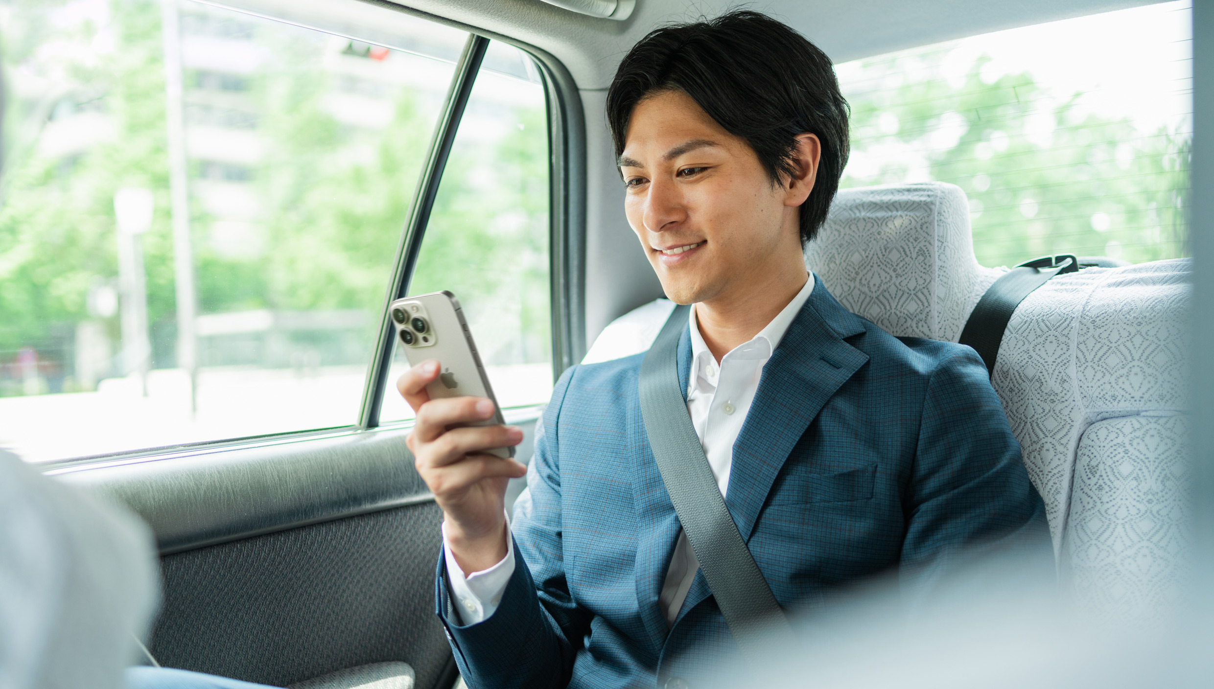A person sitting in the back seat of a car is looking at their iPhone.