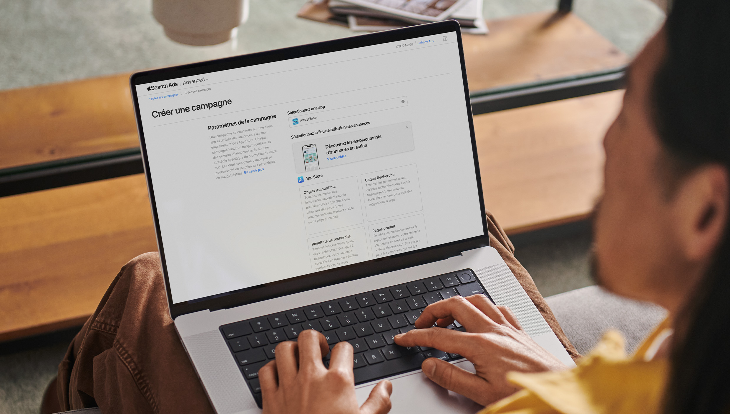 Un annonceur travaillant sur un MacBook. La page Créer une campagne d’Apple Search Ads apparaît à l’écran et présente quatre emplacements d’annonce disponibles : l’onglet Aujourd’hui, l’onglet Recherche, les résultats de la recherche et les pages produit.