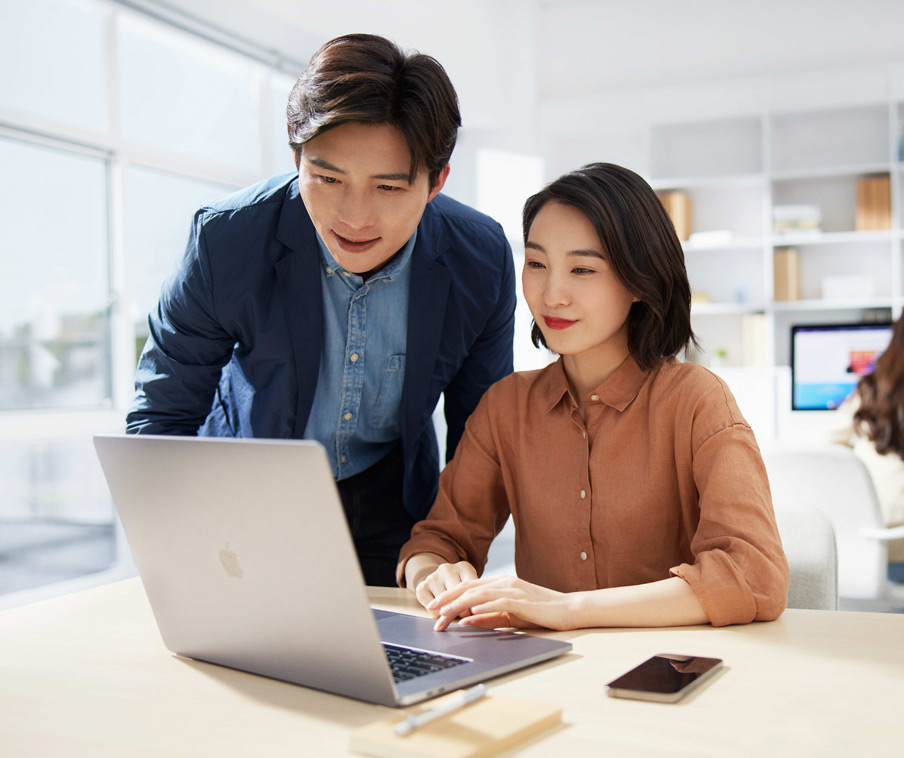 Two people working together on a MacBook.